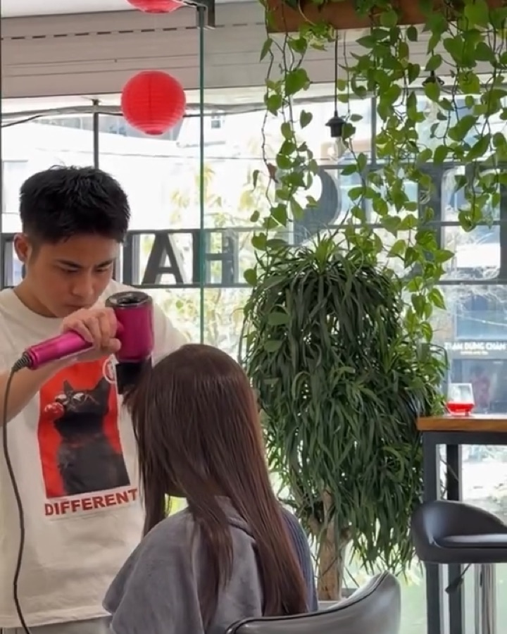Stylist sấy tạo kiểu cho khách bên mảng cây xanh và đèn lồng đỏ